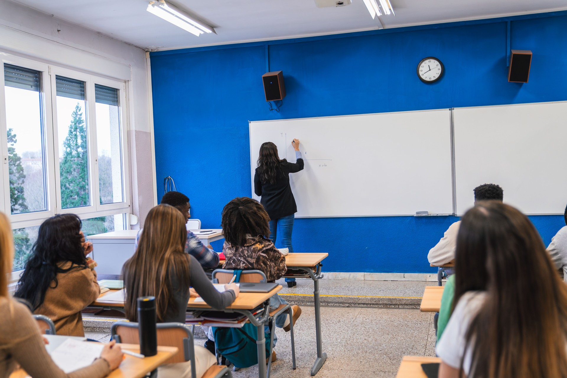 High school teacher writing on whiteboard explains lesson to diverse students